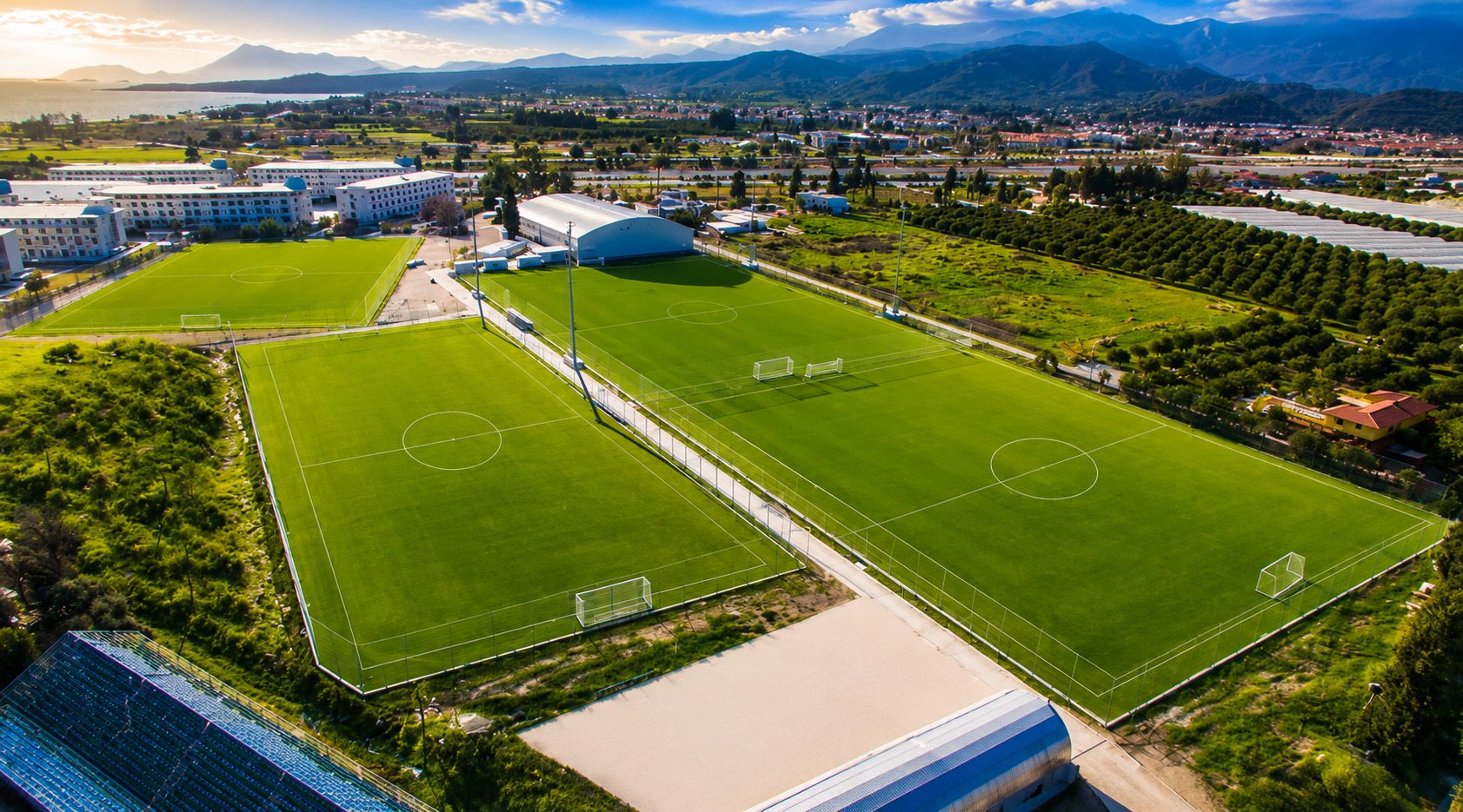 Aerial view of four football pitches at the Kemer sports complex with Mediterranean coast and mountains